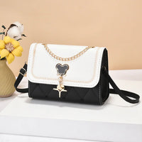 Black and white crossbody purse with gold chain, bear charm, and quilting, styled on table
