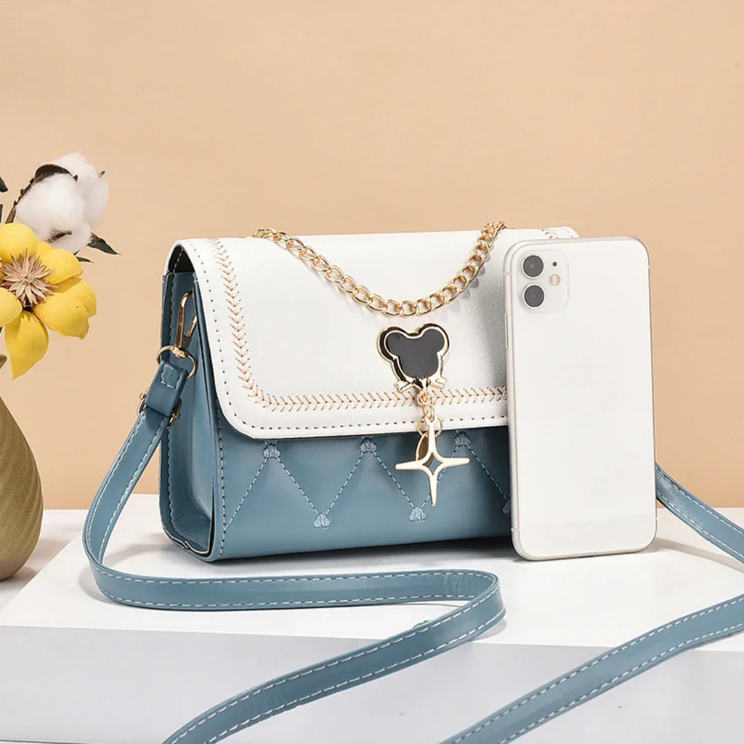 Blue and white crossbody purse with gold chain and charm, smartphone beside, flower decor