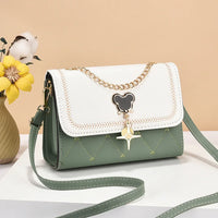 Green and white crossbody purse with gold chain and charm, displayed beside yellow flowers