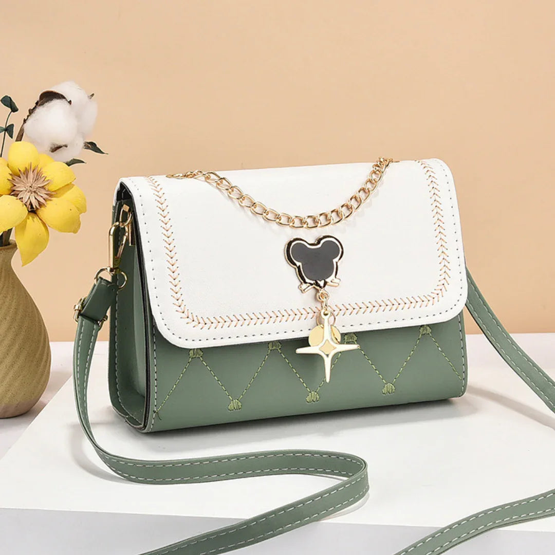 Green and white crossbody purse with gold chain and charm, displayed beside yellow flowers