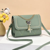 Green crossbody handbag with gold chain, bear charm, and vase with yellow flower
