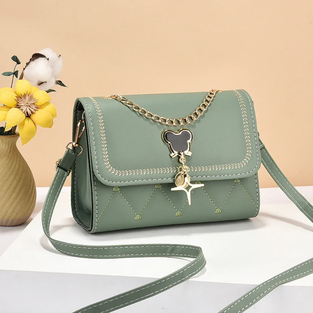 Green crossbody handbag with gold chain, bear charm, and vase with yellow flower
