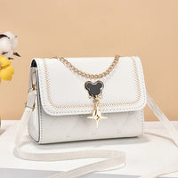 White crossbody bag with gold chain and black bear pendant, on beige background