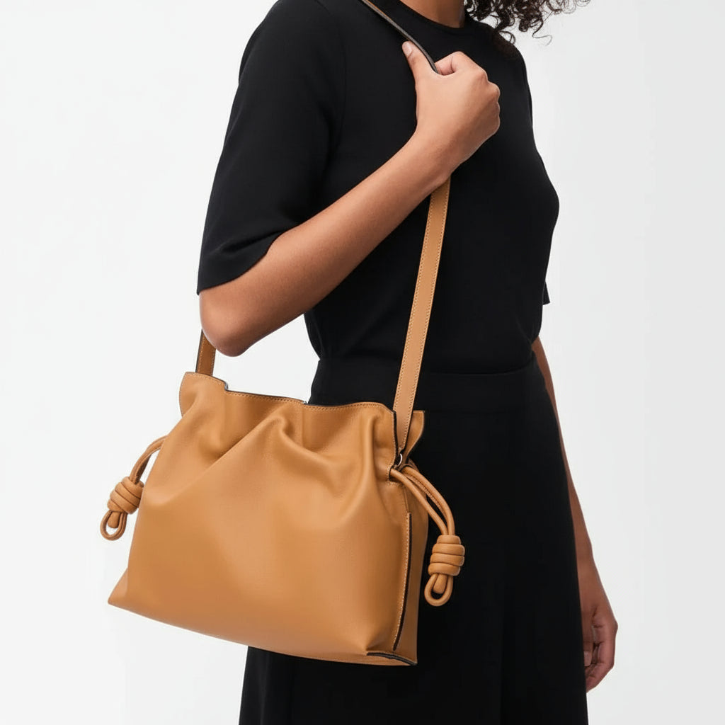 Woman in black dress holding tan leather shoulder bag with knot details