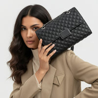 Woman in beige blazer holding black quilted leather handbag with chain strap