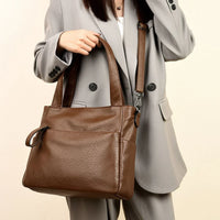 Woman in gray suit holding large brown leather tote bag with shoulder strap