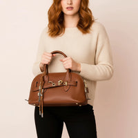 Woman holding brown leather handbag with gold hardware, wearing beige sweater