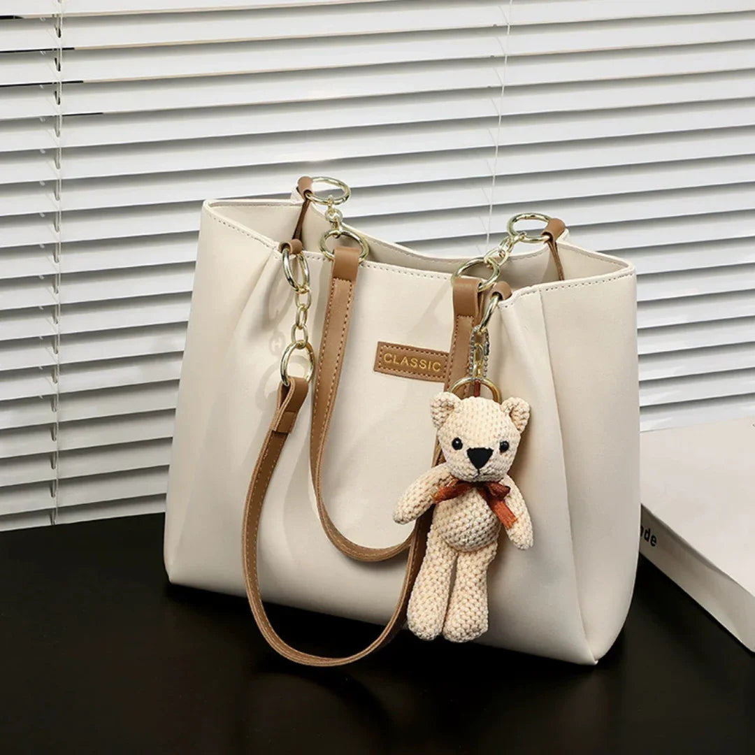 Beige tote bag with brown straps and teddy bear keychain, stylish purse on black table