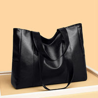 Black leather tote bag with double handles on beige background