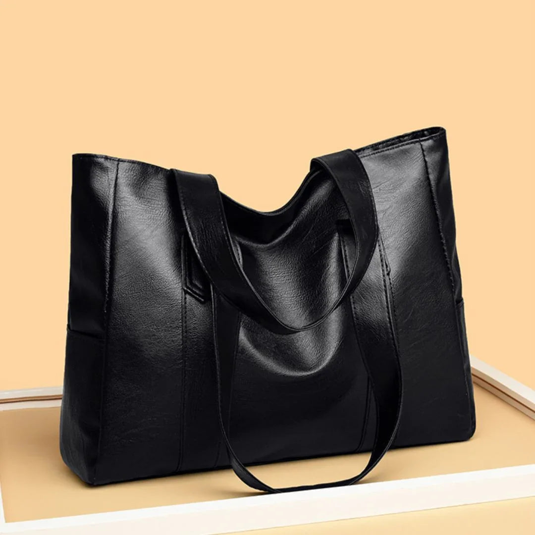 Black leather tote bag with double handles on beige background