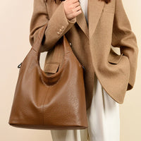 Woman in tan blazer holding large brown leather tote bag