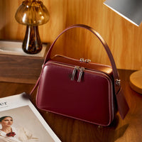 Burgundy leather handbag with top handle on wooden desk, next to lamp and magazine