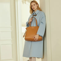 Woman in light blue coat holding large tan leather tote bag in modern interior