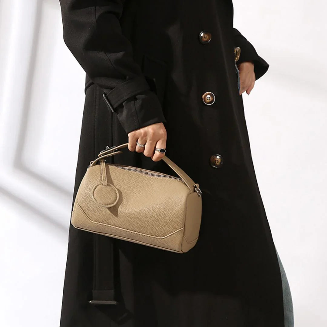 Woman in black coat holding beige leather handbag with zipper and round tag