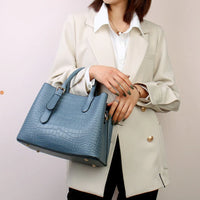 Woman in beige blazer holding blue crocodile pattern tote handbag