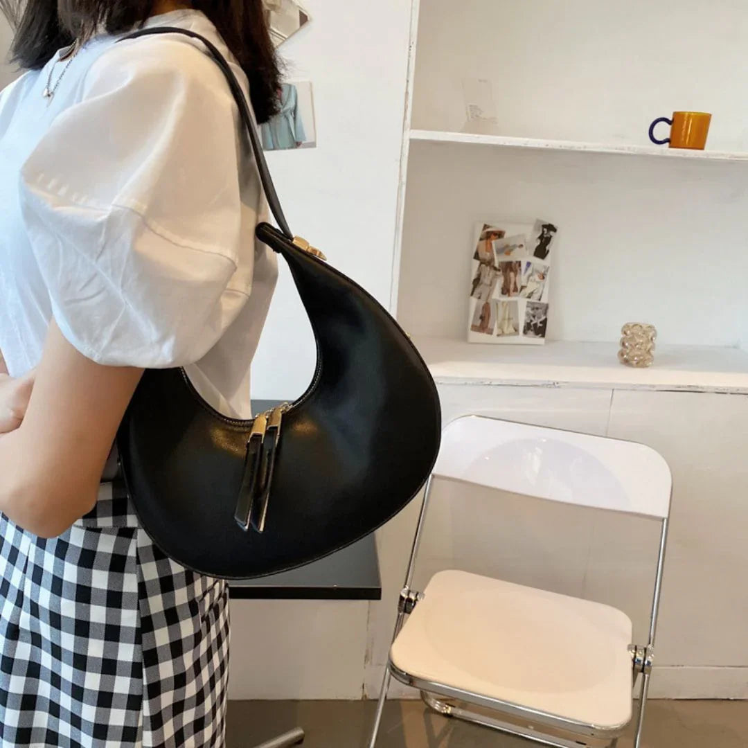 Woman wearing white puff sleeve top, checkered skirt, and black crescent shoulder bag indoors