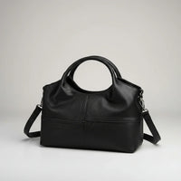 Black leather handbag with round handles and detachable shoulder strap on a white background