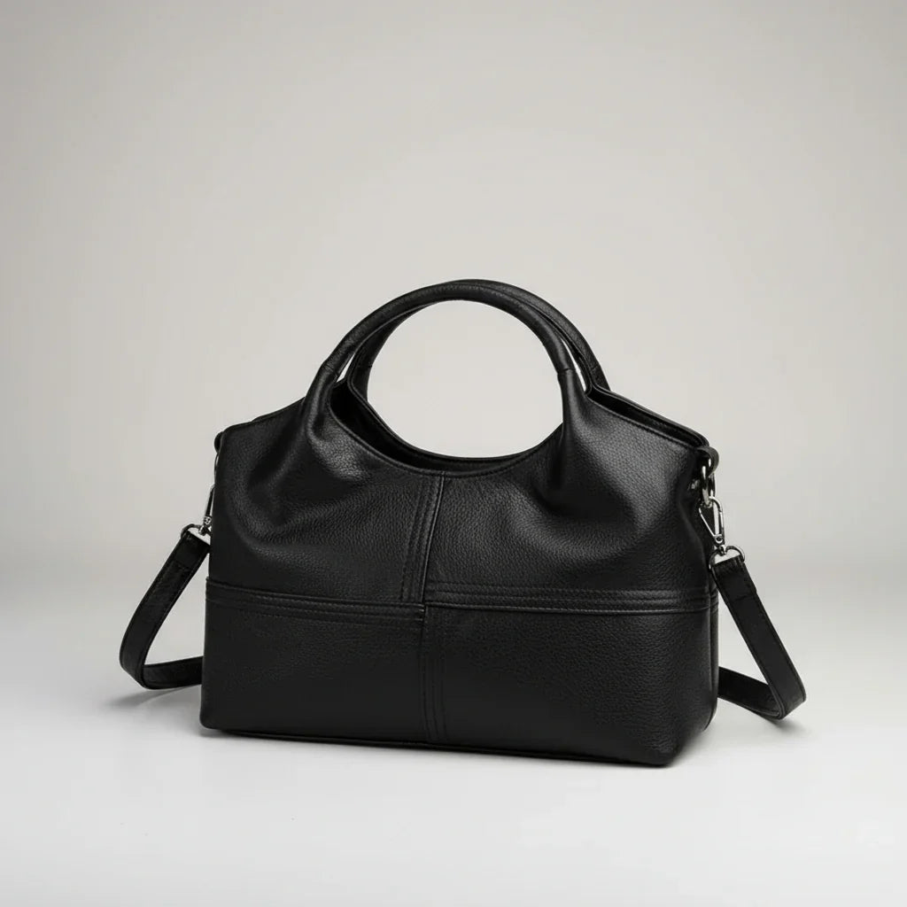 Black leather handbag with round handles and detachable shoulder strap on a white background