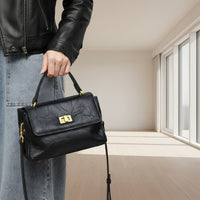 Woman holding black leather handbag with gold clasp, wearing black jacket and jeans