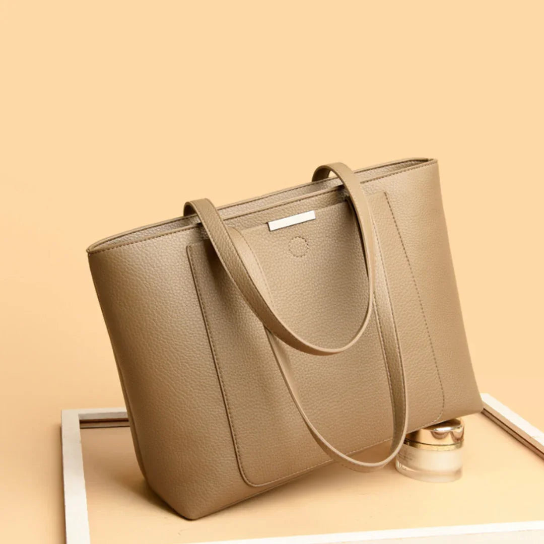 Taupe leather tote bag with double handles on a beige background, stylish womens handbag