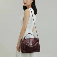 Woman in white dress holding burgundy leather handbag with top handle and shoulder strap