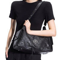 Woman in black shirt carrying a large black leather shoulder bag with logo emblem