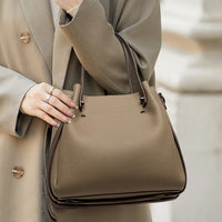 Woman in beige coat holding taupe leather handbag, minimalist fashion accessory