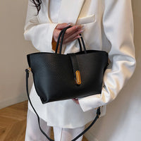 Woman in white suit holding black leather handbag with gold accent and shoulder strap