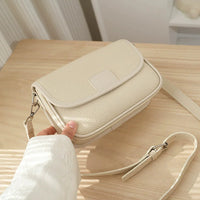 Beige leather crossbody bag with textured finish on light wooden table