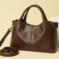 Brown leather handbag with top handles and detachable strap on beige background