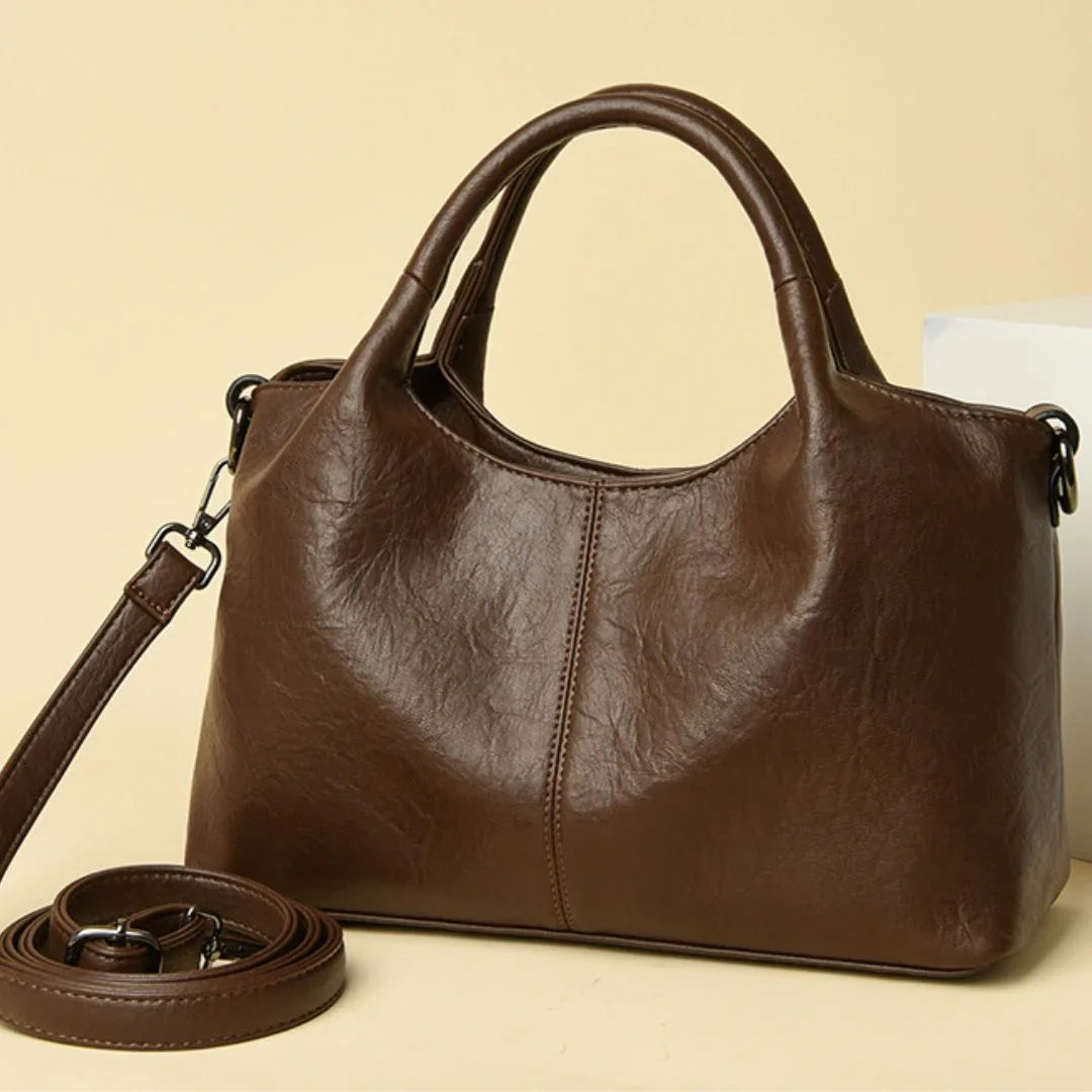 Brown leather handbag with top handles and detachable strap on beige background