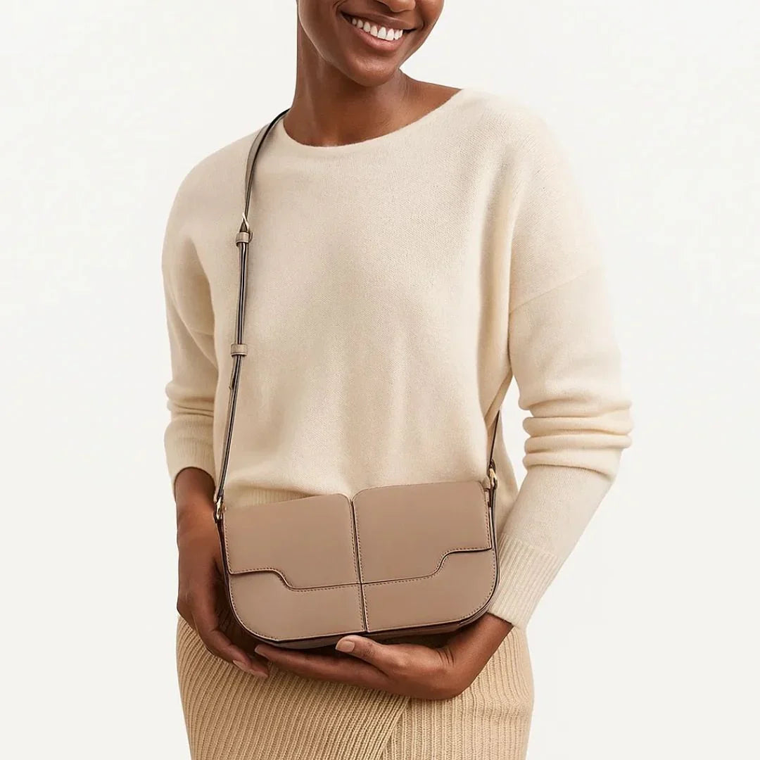Woman in cream sweater with beige crossbody leather handbag against neutral background