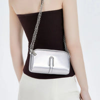 Woman wearing a silver crossbody purse with chain strap, black top and white pants