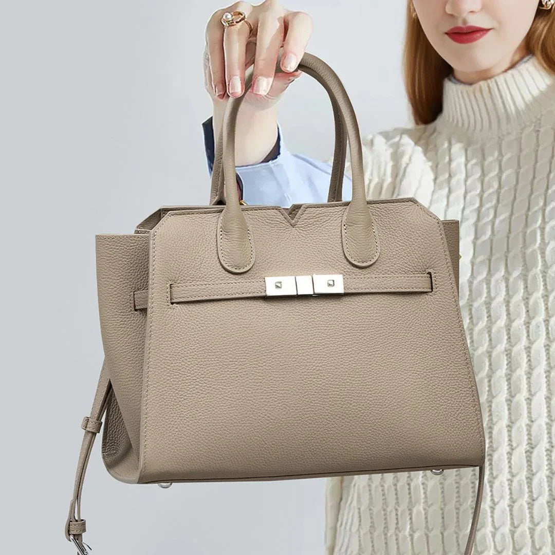 Woman holding taupe leather tote handbag with top handles and silver clasp