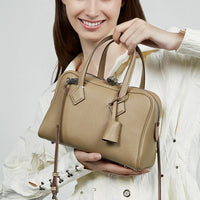 Woman in white shirt holding a beige leather handbag with double handles and zipper.