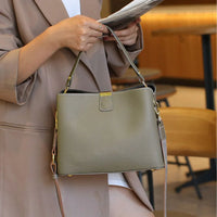 Woman in beige coat holding olive green leather handbag with gold hardware in cafe