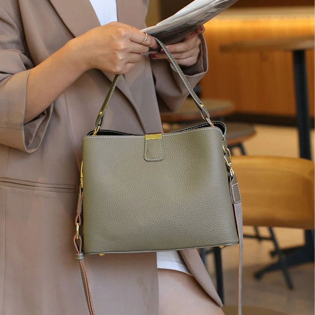 Woman in beige coat holding olive green leather handbag with gold hardware in cafe