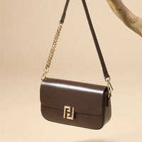 Brown leather shoulder bag with gold chain strap and logo clasp, hanging on a branch