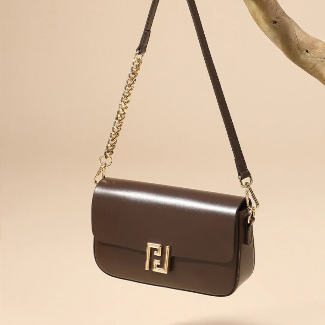 Brown leather shoulder bag with gold chain strap and logo clasp, hanging on a branch