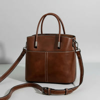 Brown leather handbag with handles and adjustable strap on white background