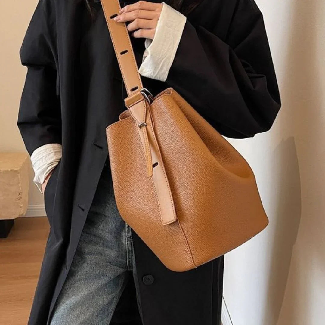 Woman wearing black coat and jeans carrying a brown leather bucket bag