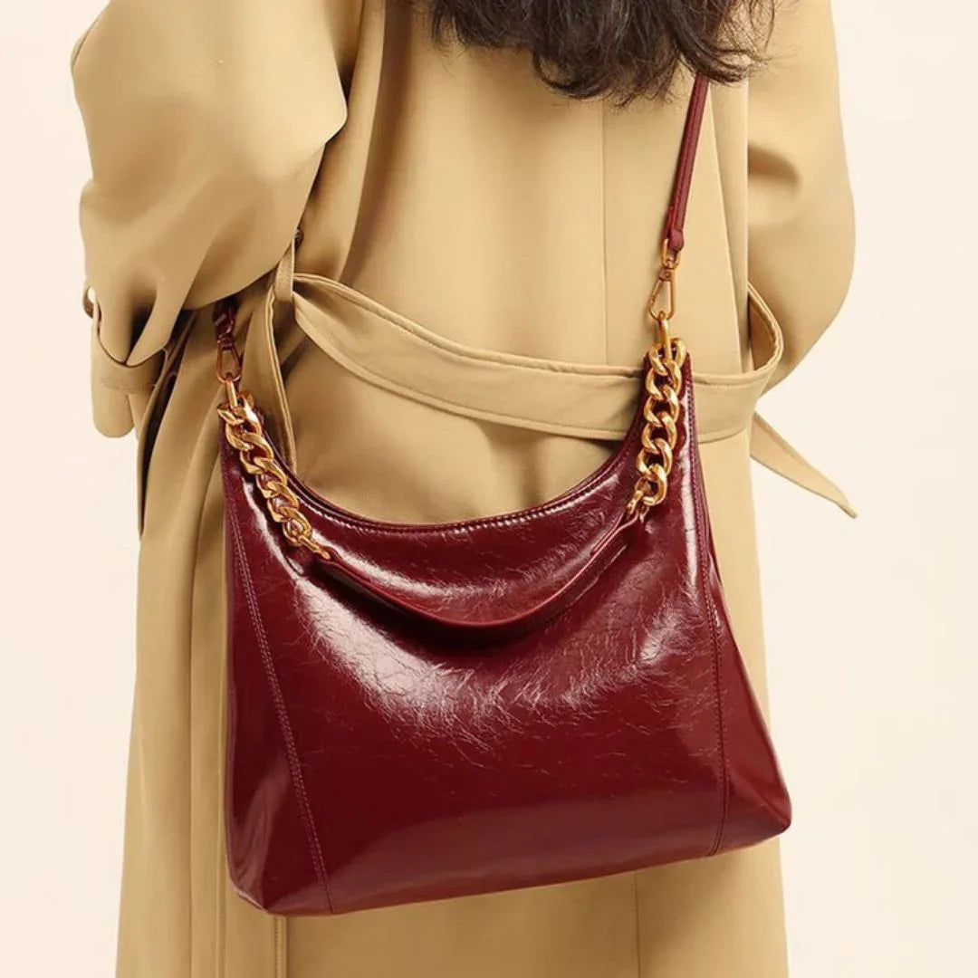 Burgundy leather shoulder bag with gold chain strap on beige trench coat