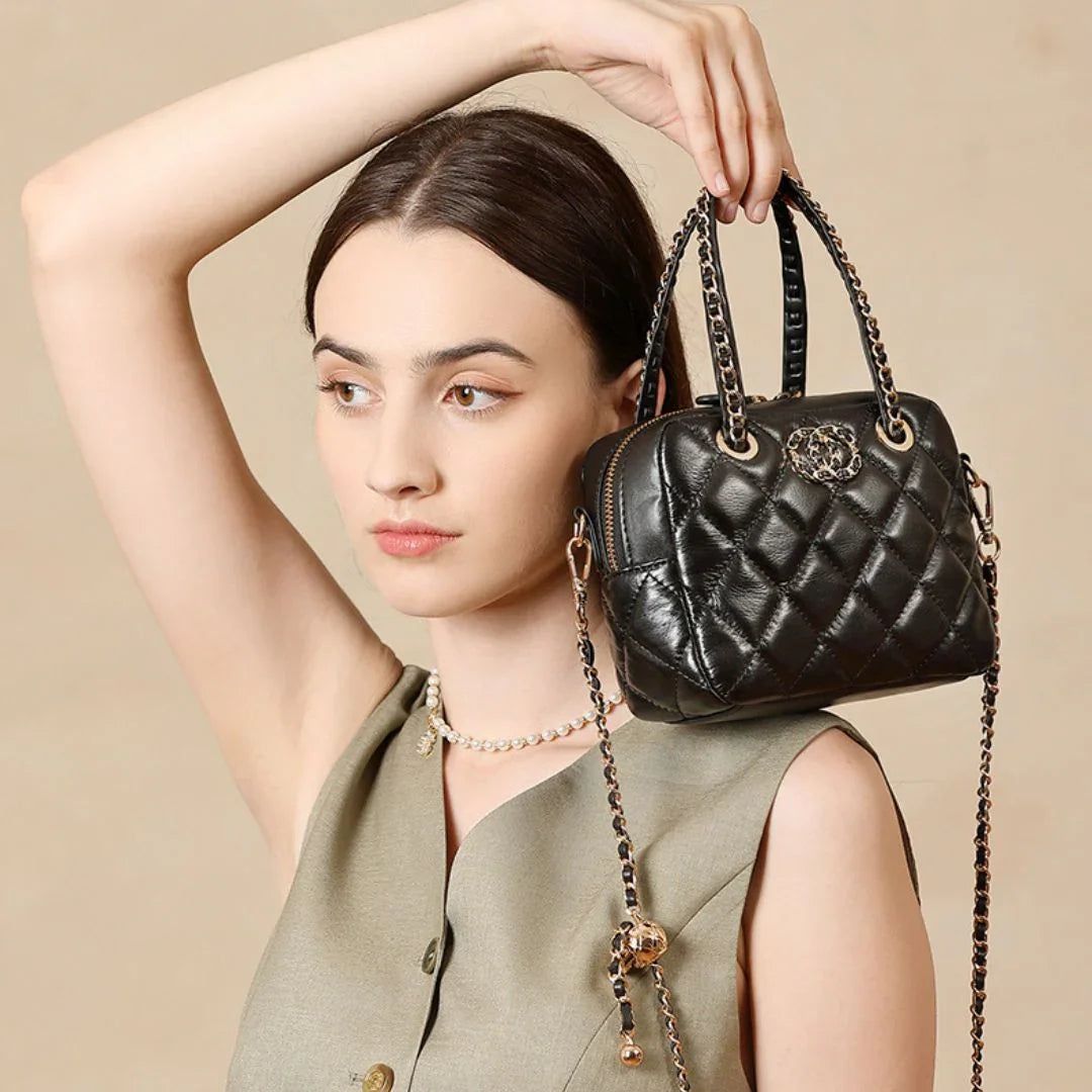 Woman in beige top holding black quilted leather handbag with chain strap