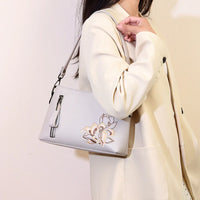 Woman in cream blazer carrying light gray floral embroidered shoulder bag