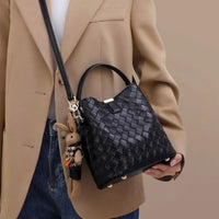 Woman in beige blazer holds black woven leather handbag with bunny keychain