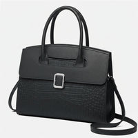 Elegant black leather handbag with crocodile texture and silver buckle on white background