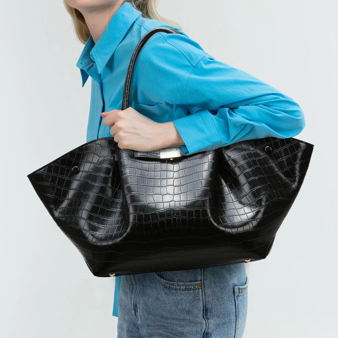 Woman wearing blue shirt and jeans carrying large black crocodile-embossed tote bag