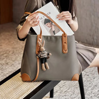 Taupe leather tote bag with brown straps, bunny keychain, magazine, and woman's hands