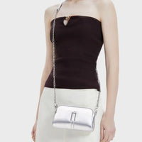 Woman wearing a metallic silver crossbody bag with chain strap and a dark one-shoulder top