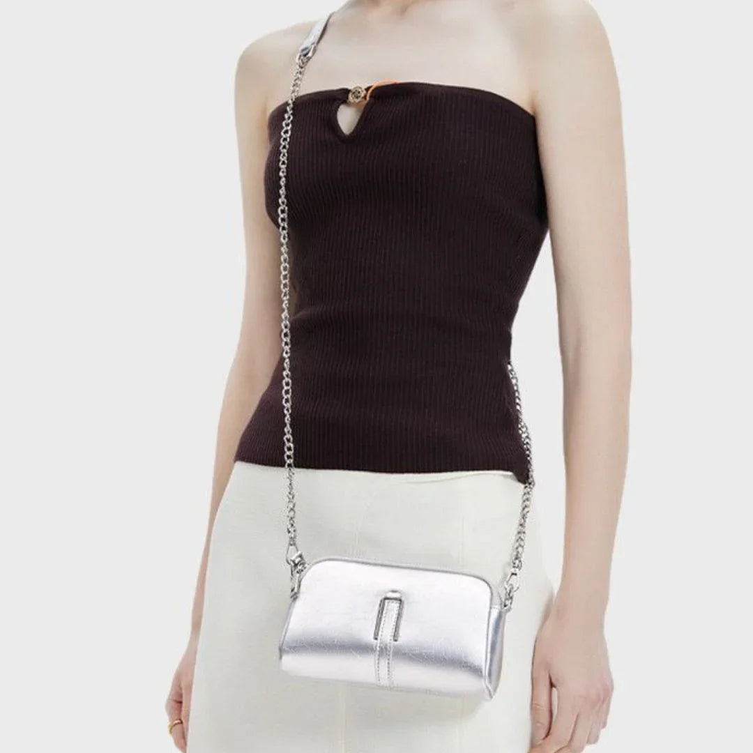 Woman wearing a metallic silver crossbody bag with chain strap and a dark one-shoulder top